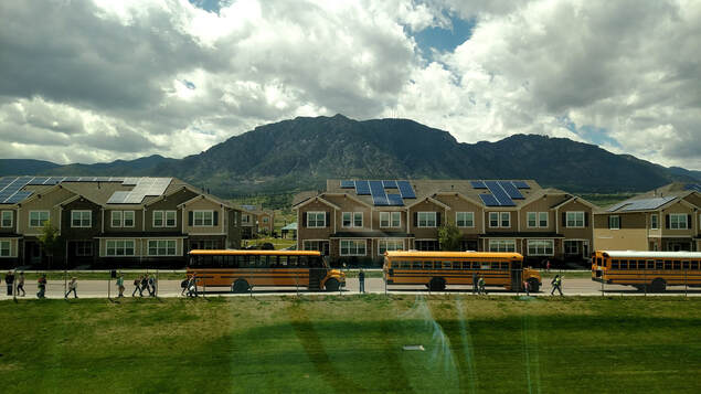 School buses picking up kids with a mountain in the background
